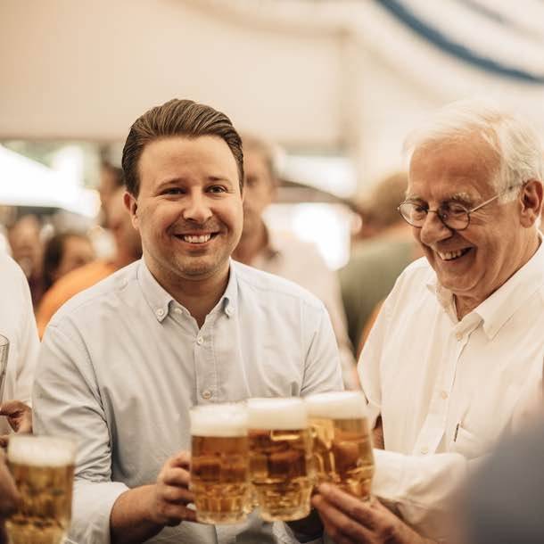 Zwei Männer stoßen mit Biergläsern in einer fröhlichen Runde an.