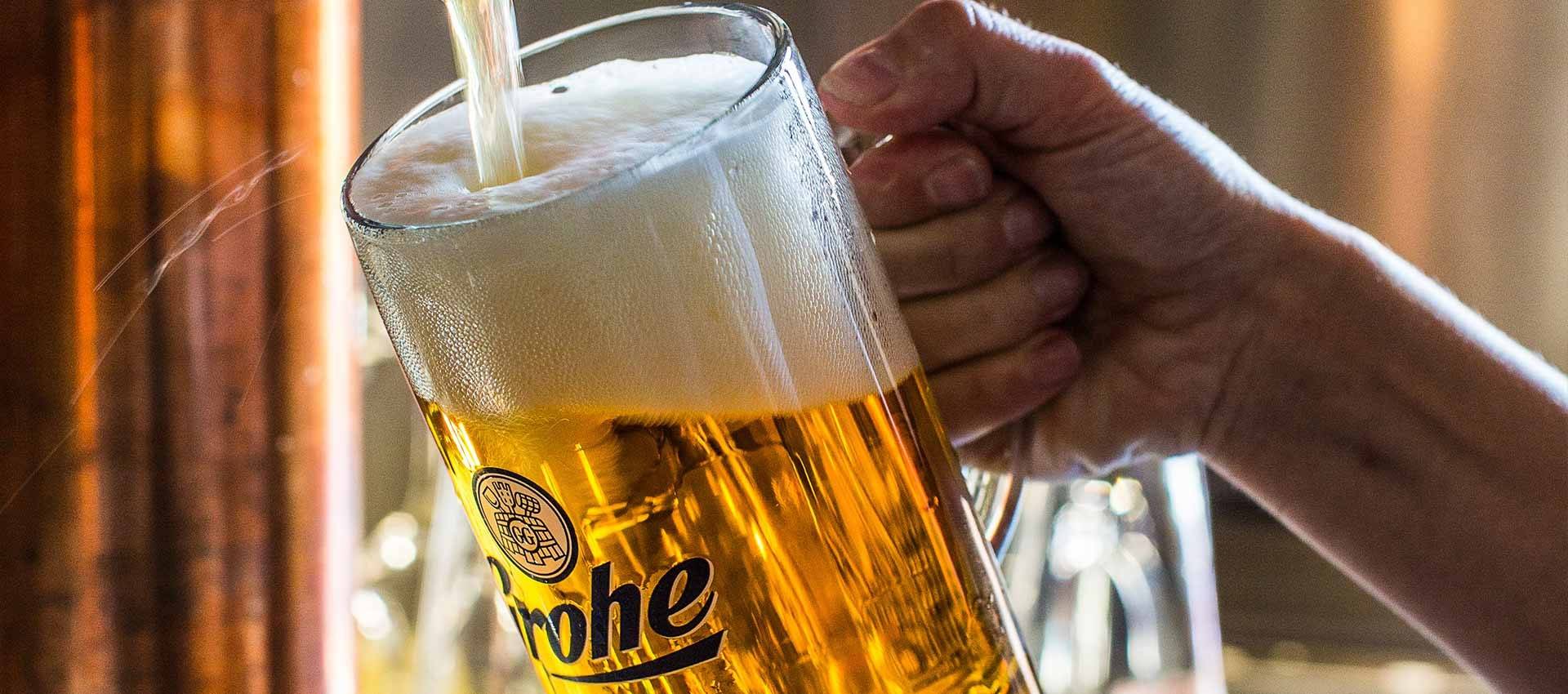 Nahaufnahme einer Hand, die einen großen Bierkrug hält, in den frisches Bier mit Schaum eingegossen wird.