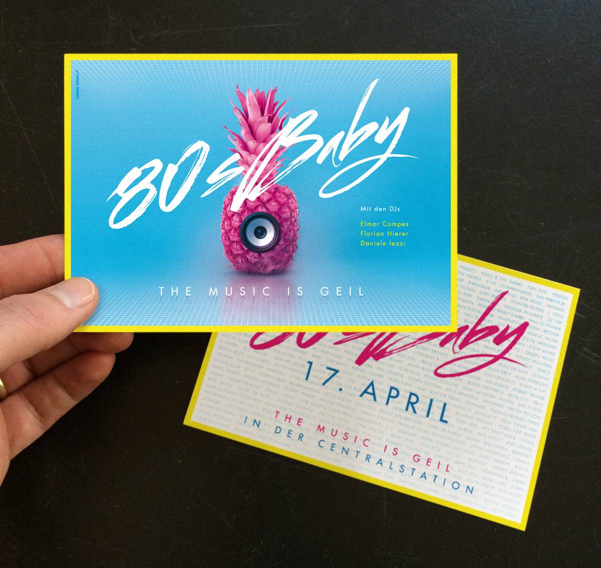 Zwei bunte Einladungskarten für eine 80s-Party, eine davon wird in der Hand gehalten; darauf eine pinke Ananas mit Lautsprecher und der Text „80s Baby – The Music is Geil“.