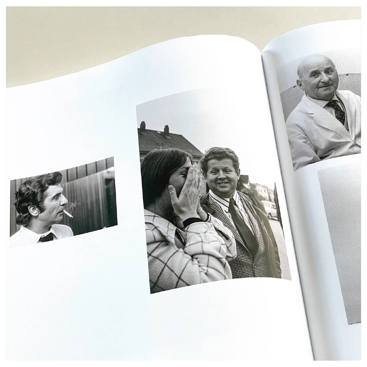 Aufgeschlagenes Fotobuch mit drei Schwarzweißfotos: ein Mann mit Zigarette im Mund, eine lachende Frau mit Händen vor dem Gesicht neben einem Mann im Anzug, und ein älterer Mann im weißen Kittel.