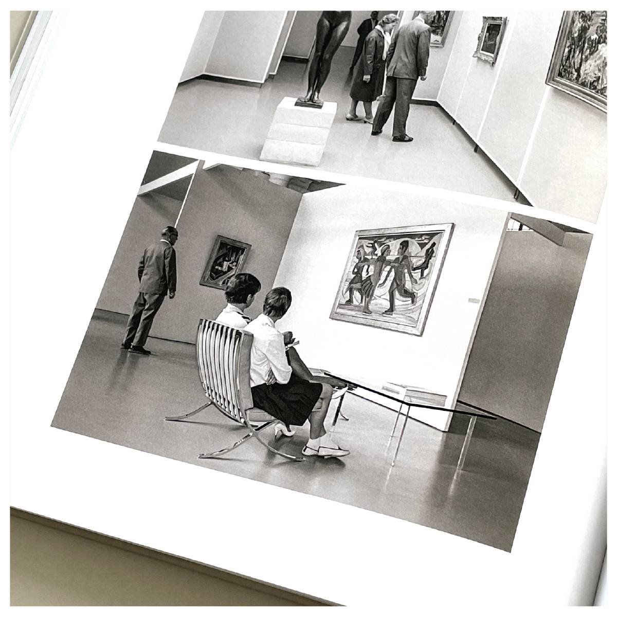 Zwei schwarz-weiß Fotos in einem Buch zeigen Menschen, die Kunst in einer Galerie betrachten; auf dem oberen Foto betrachten drei Personen eine Skulptur und Gemälde, auf dem unteren sitzen zwei Personen auf Stühlen vor einem Gemälde, während ein Mann umhergeht.