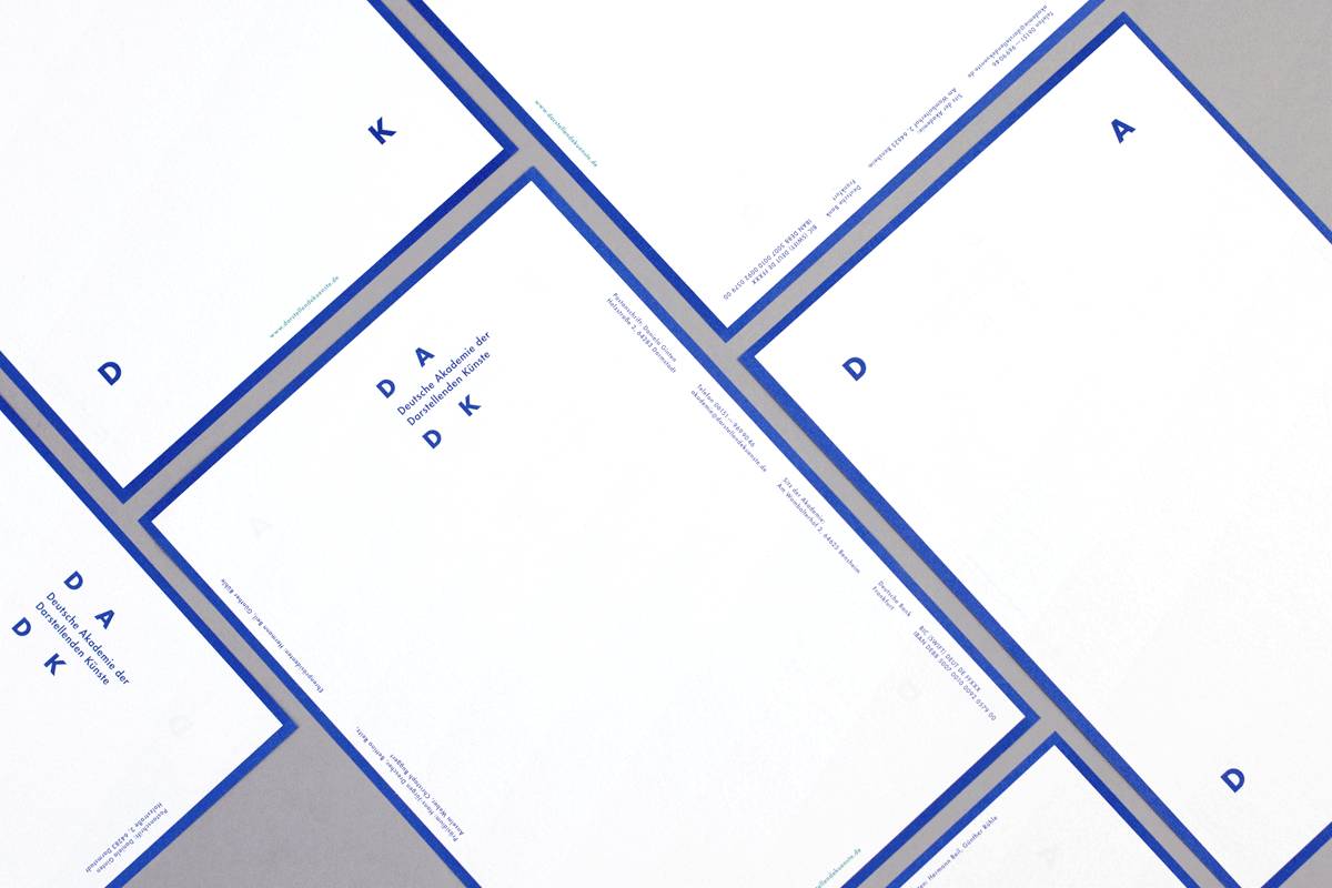 Mehrere weiße Briefbögen mit blauen Rändern und minimalistischer blauer Beschriftung, darauf die Initialen „DADDK“ und der Schriftzug „Deutsche Akademie der Darstellenden Künste“.