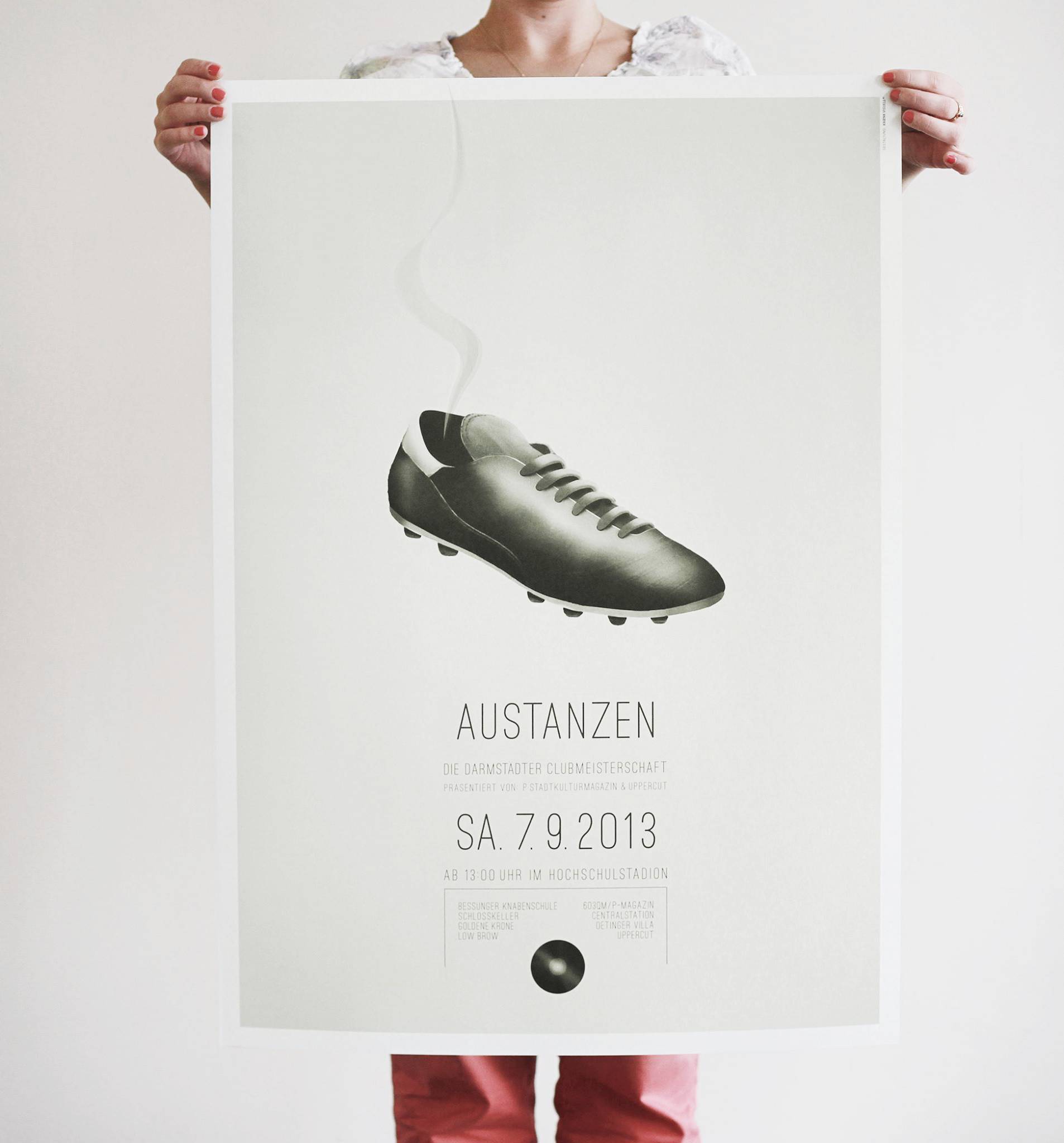 Person hält ein Plakat mit einem schwarzen Fußballschuh, aus dem Rauch aufsteigt; darunter stehen Informationen zu einer Veranstaltung namens „AUSTANZEN“ am 7.9.2013.