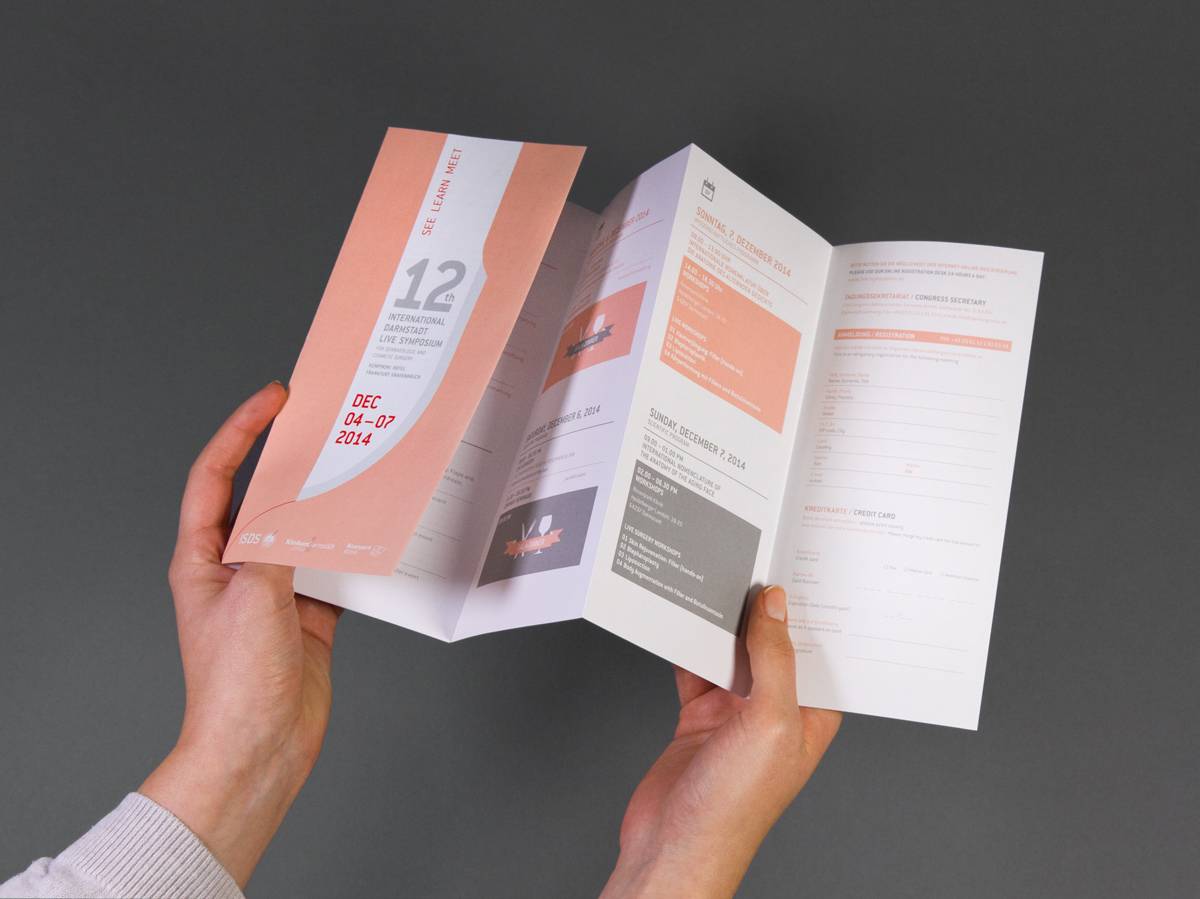 Zwei Hände halten einen aufgeklappten, mehrseitigen Flyer mit Text und grafischen Elementen in Rosa, Weiß und Grau.