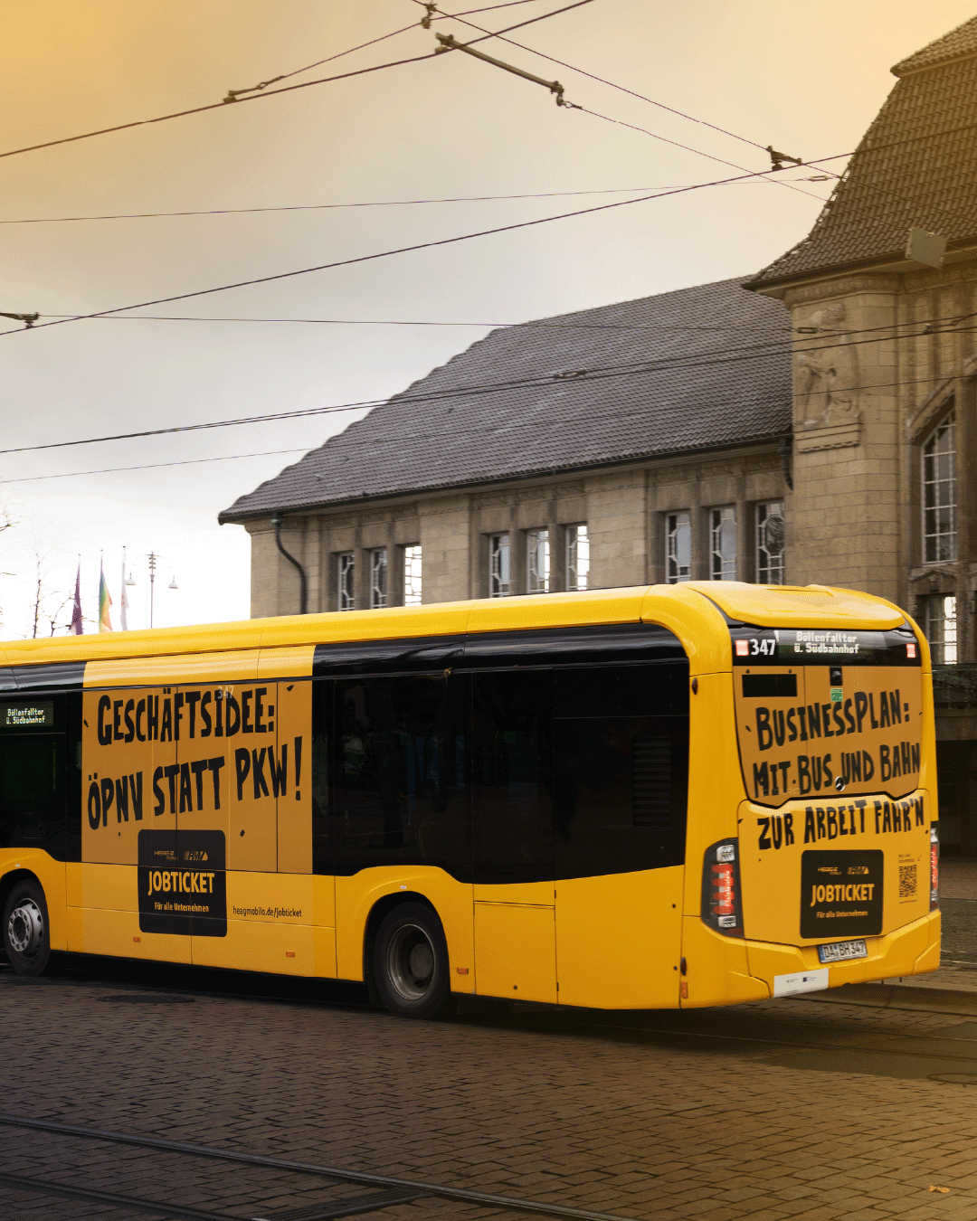 Gelber Linienbus mit großflächiger Werbeaufschrift für das Jobticket: „Geschäftsidee: ÖPNV statt PKW!“ und „Businessplan: Mit Bus und Bahn zur Arbeit fahren“. Im Hintergrund ein historisches Gebäude.