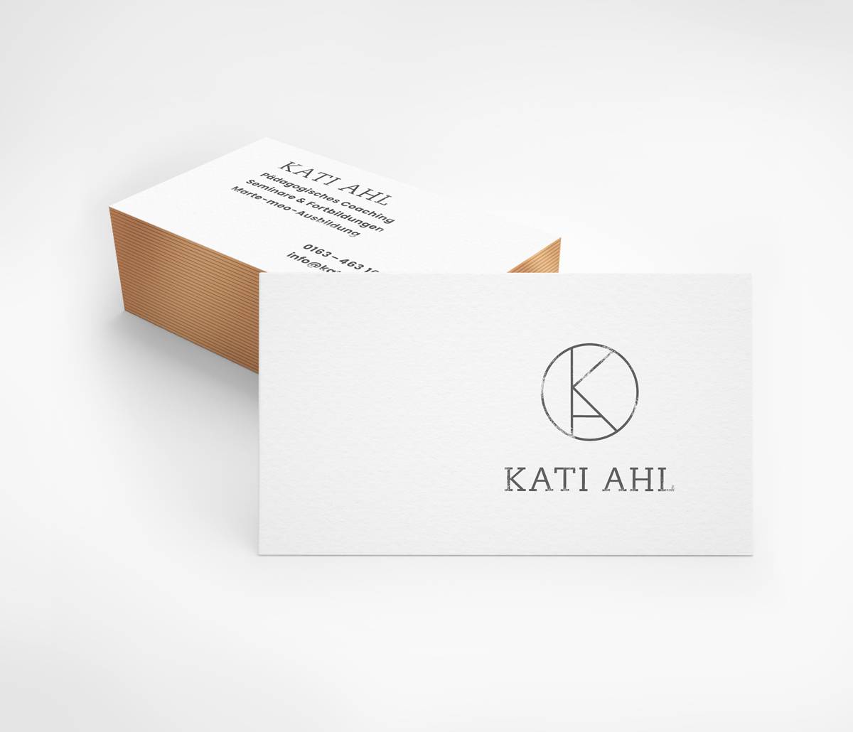 Ein Stapel schlichter, weißer Visitenkarten mit schwarzer Schrift; auf der Vorderseite sind ein rundes Logo mit dem Buchstaben "K" und der Name "KATI AHL" zu sehen.