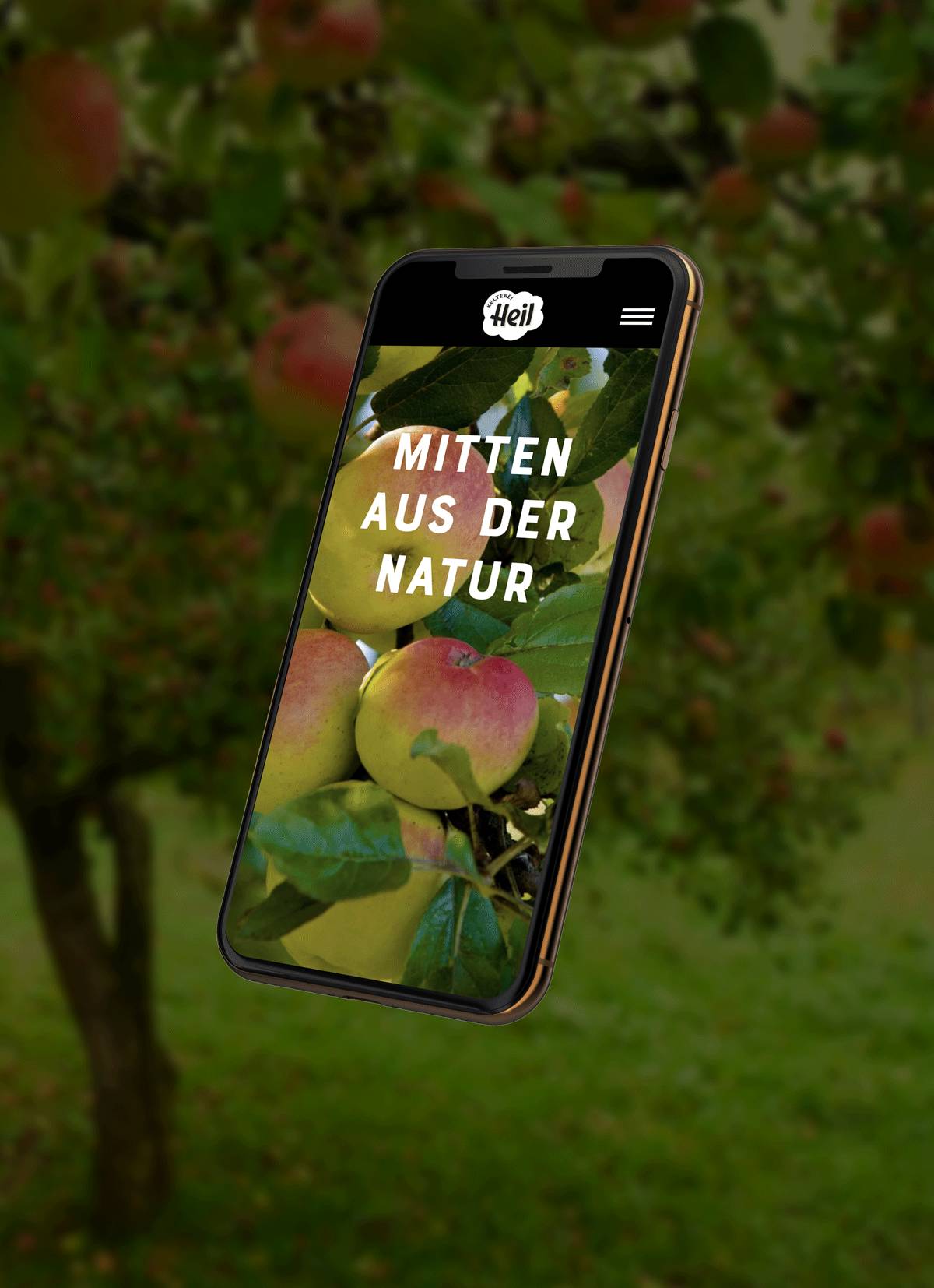Ein Smartphone schwebt vor einem Apfelbaum; auf dem Display sind Äpfel und der Text "MITTEN AUS DER NATUR" zu sehen.