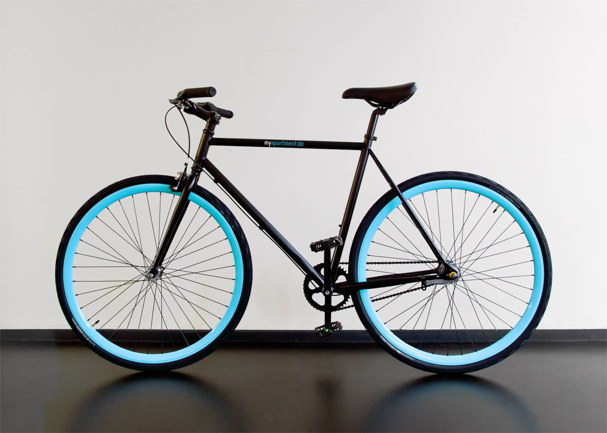 Schwarzes Fahrrad mit himmelblauen Felgen steht vor einer weißen Wand.