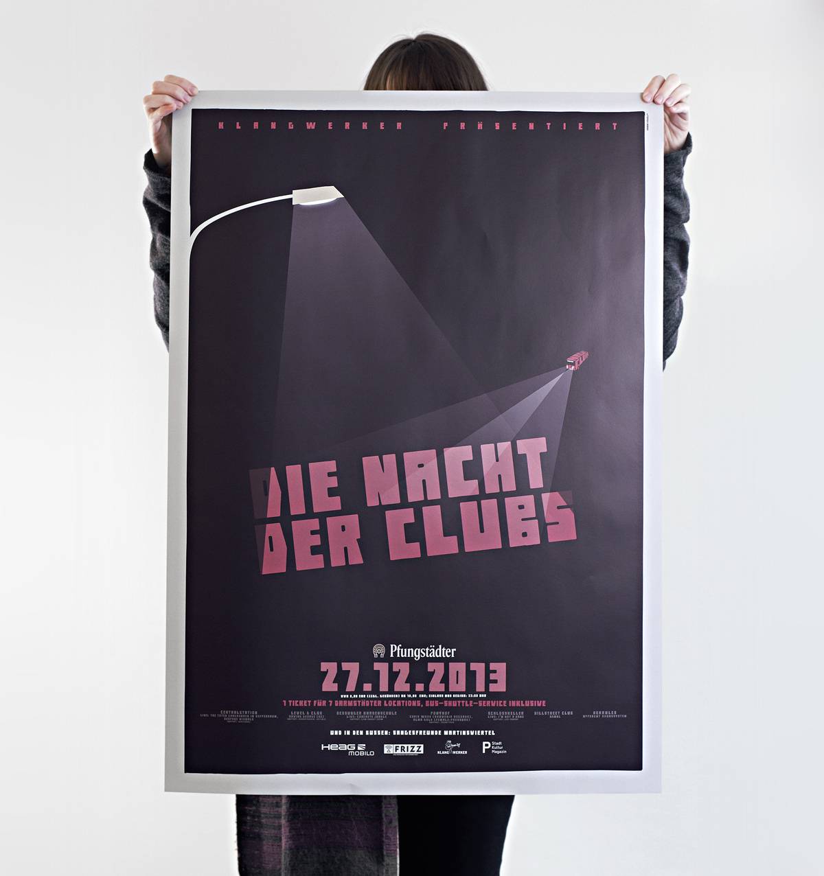 Person hält ein großes Plakat mit schwarzem Hintergrund, darauf steht in großen rosa Buchstaben "Die Nacht der Clubs" und darunter das Datum "27.12.2013".