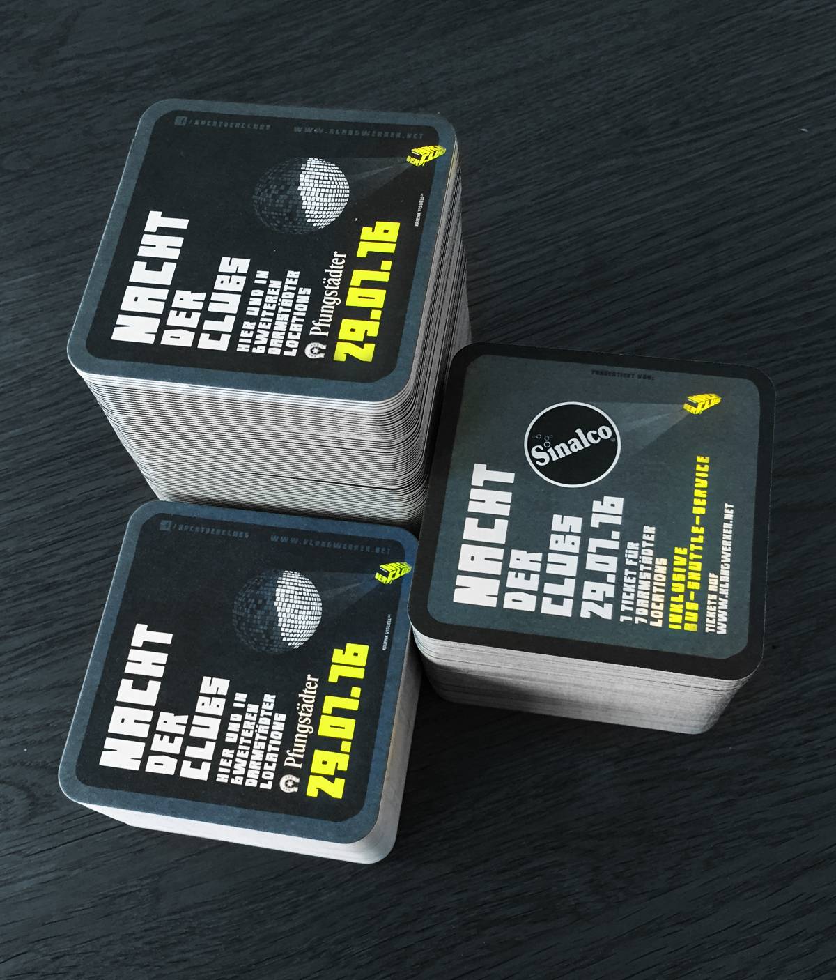 Drei Stapel quadratischer Bierdeckel mit schwarzem Design und weiß-gelber Schrift, die für die Veranstaltung "Nacht der Clubs" am 29.01.16 werben.