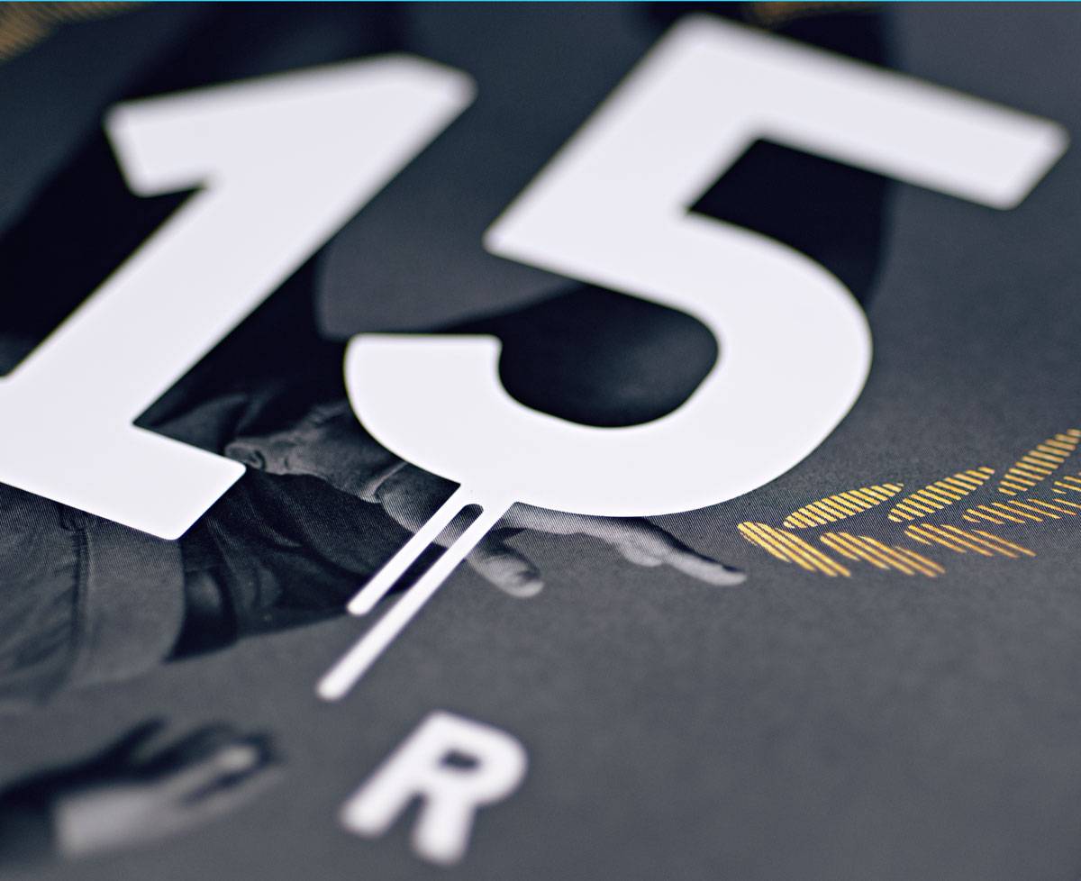 Große weiße Zahl 15 mit kleinem Buchstaben R auf dunklem Hintergrund, teilweise über einem Foto von Händen und goldenen Linien.