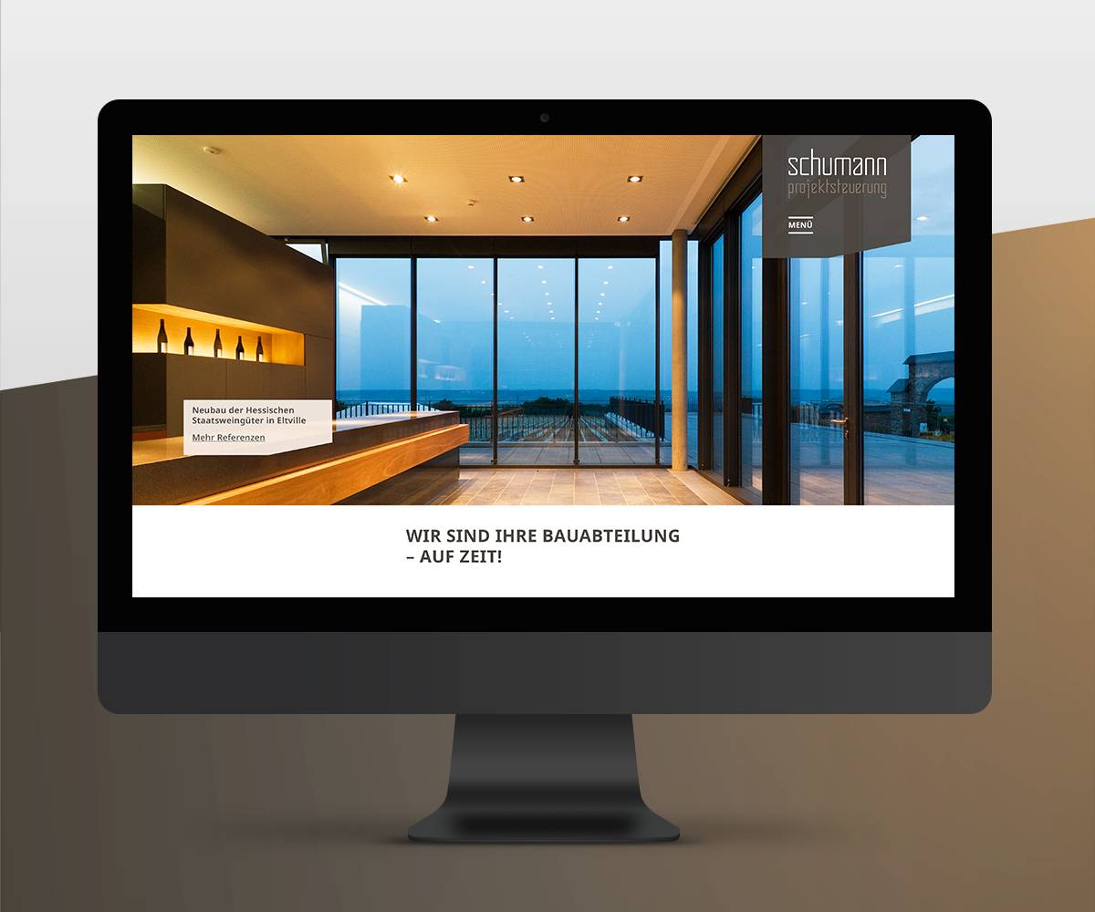 Monitor mit geöffneter Website, die ein modernes Gebäude mit großen Glasfronten zeigt; Text: „Wir sind Ihre Bauabteilung – auf Zeit!“ und „schumann projektsteuerung“.