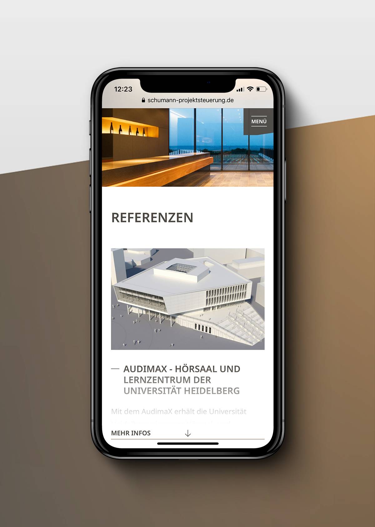 Smartphone mit geöffneter Webseite, die ein Referenzprojekt (Audimax Universität Heidelberg) mit Bild eines modernen Gebäudes zeigt.
