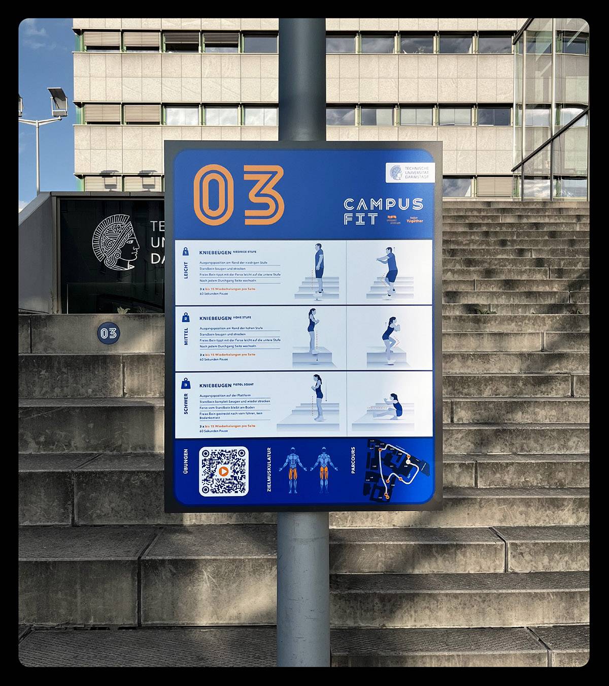 Fitness-Infotafel mit Trainingsanleitung für Kniebeugen in drei Schwierigkeitsgraden, illustriert mit Grafiken und Text, aufgestellt vor einer Treppe an einem Universitätscampus.