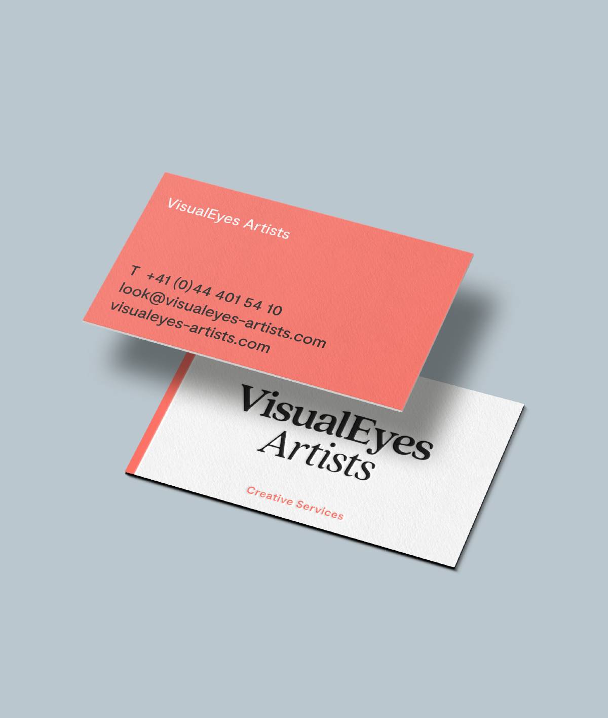 Zwei übereinanderliegende Visitenkarten auf hellgrauem Hintergrund; die obere Karte ist korallenrot mit Kontaktdaten, die untere weiß mit schwarzem Logo „VisualEyes Artists“ und rotem Text „Creative Services“.